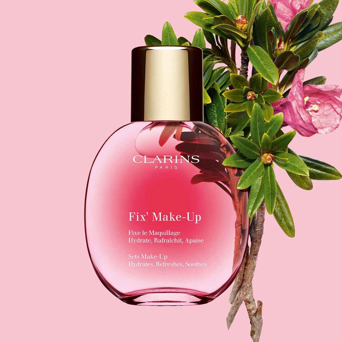 Foto del envase del spray fijador de maquillaje de Clarins al lado de un ramo de rosas con un fondo blanco