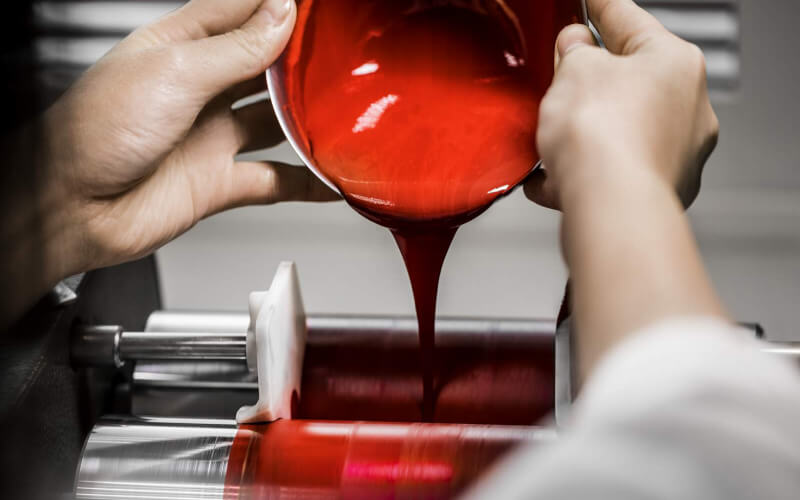 Un técnico vierte una preparación cremosa de maquillaje rojo en una máquina