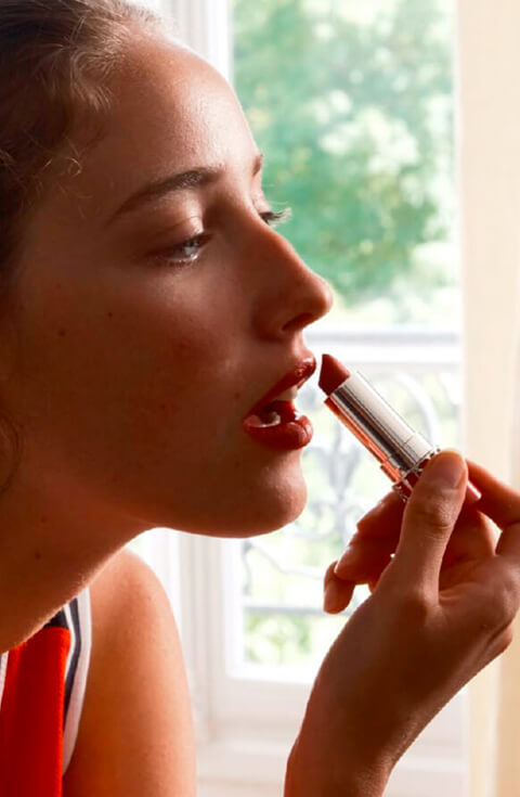 Mujer joven maquillándose delante del espejo con la barra de labios Joli Rouge
